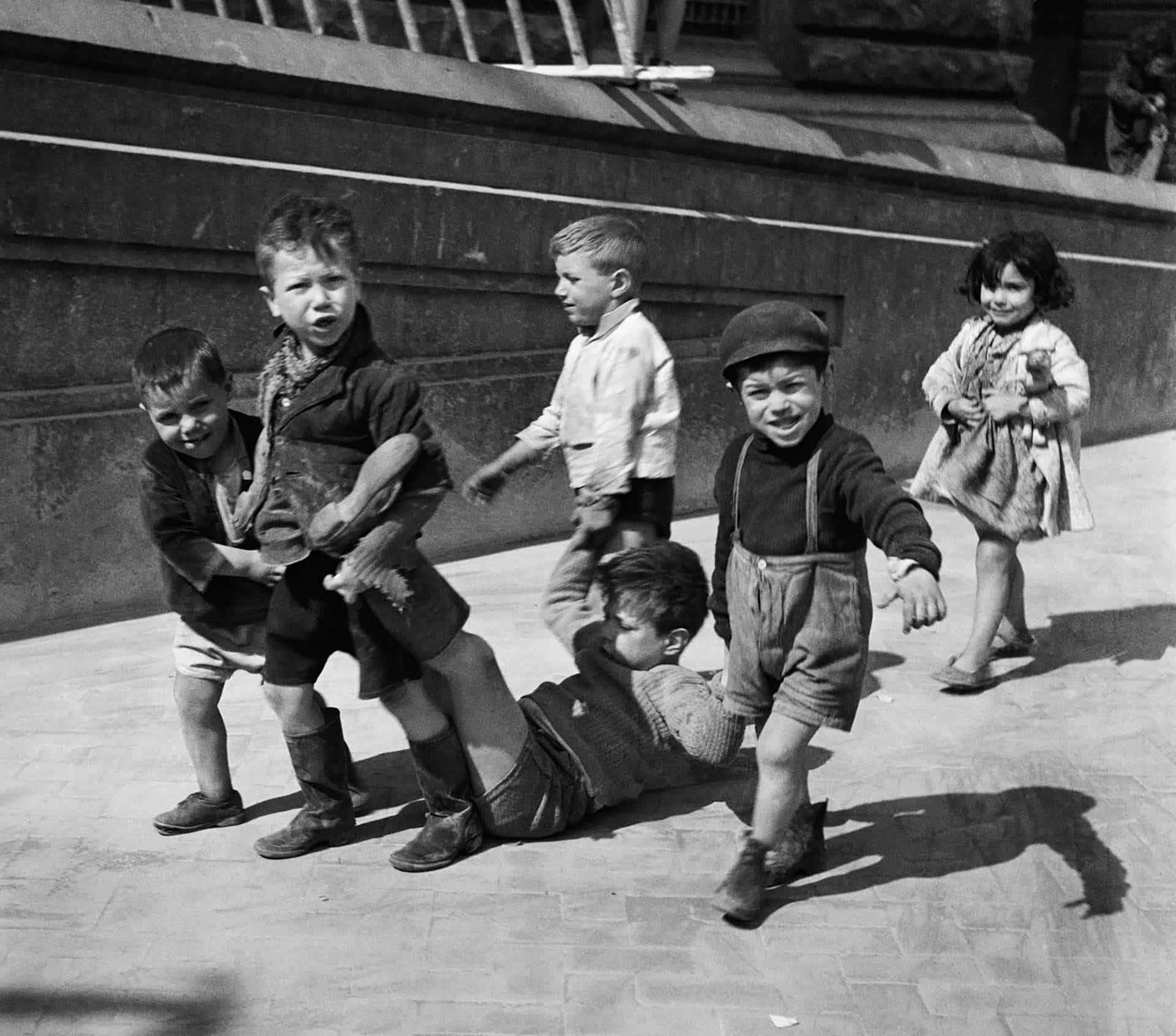 Willy Ronis portant un enfant dans la rue, entouré d’un groupe d’enfants à Paris dans les années 1950